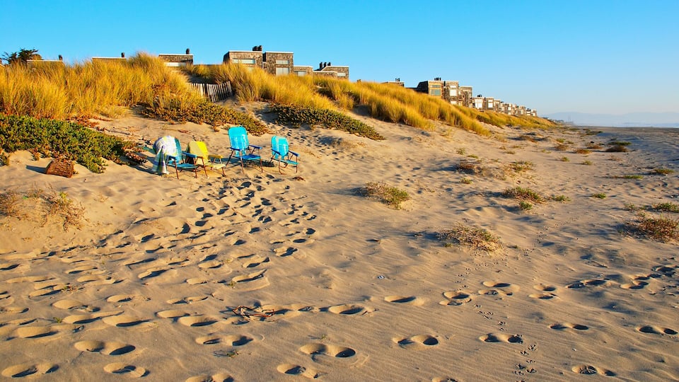 A sandy beach with footprints, a dune, and a row of beach chairs.