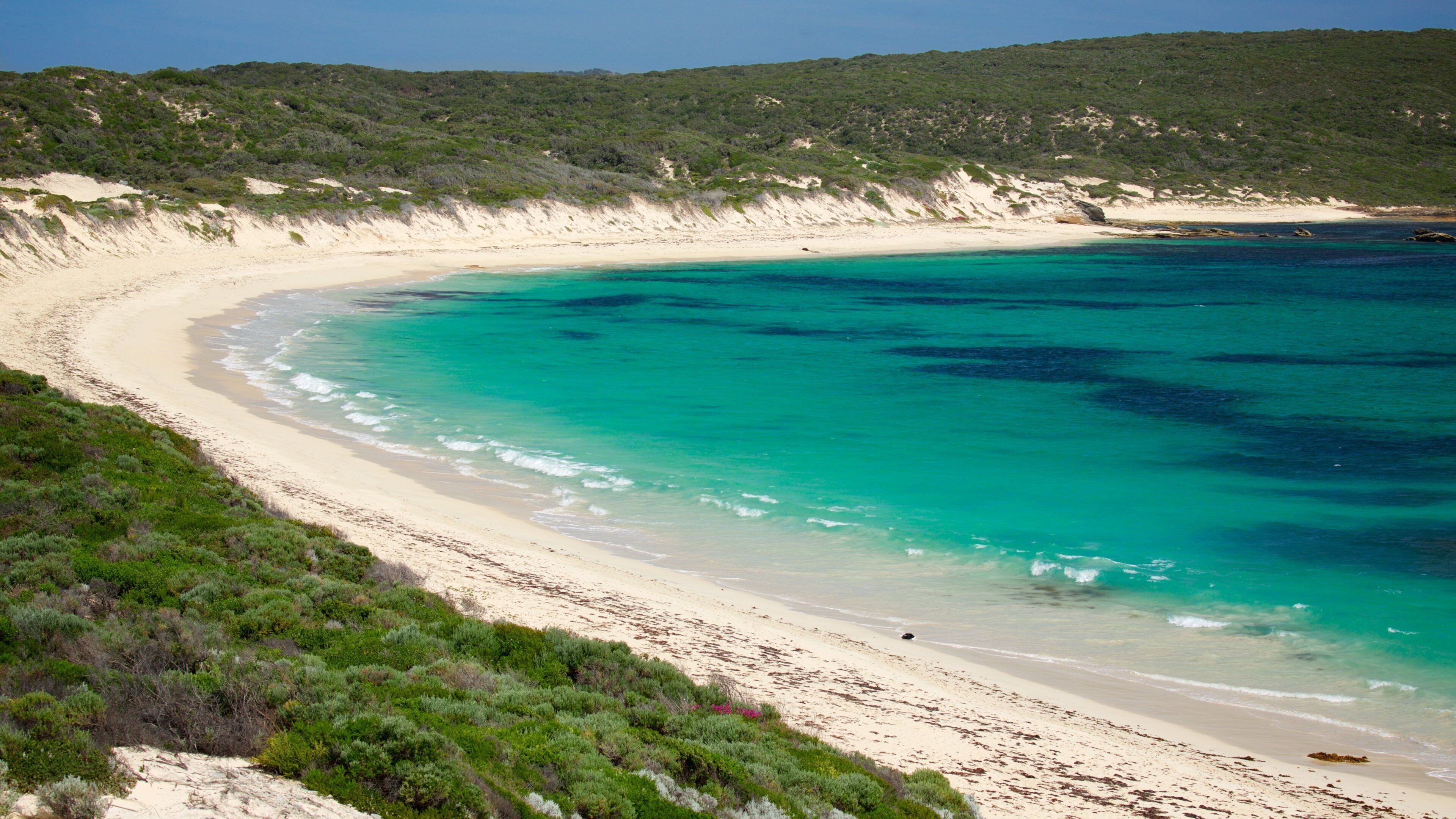 A curved sandy beach with turquoise waters and green vegetation.