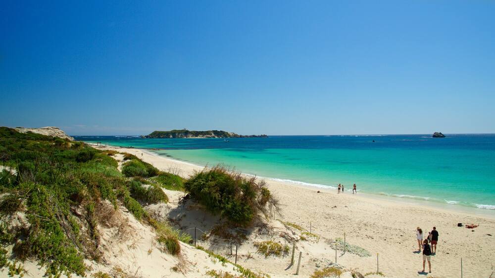 A beach with clear turquoise waters, sandy shores, and a small island in the distance.
