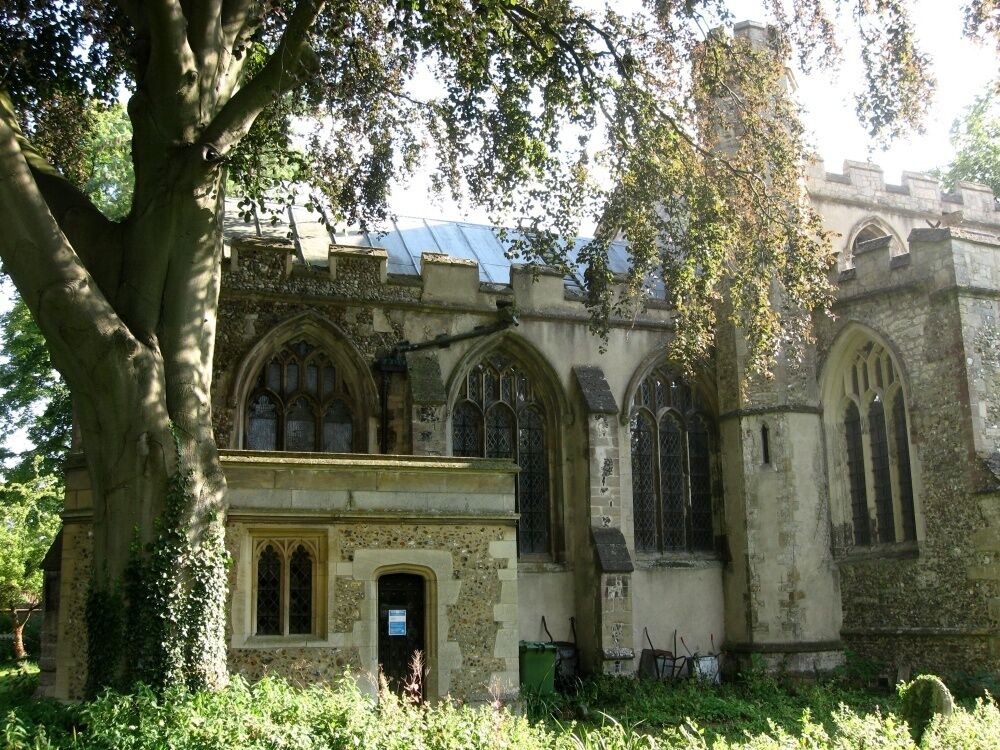 An old church with Gothic architecture, surrounded by trees and overgrown vegetation.