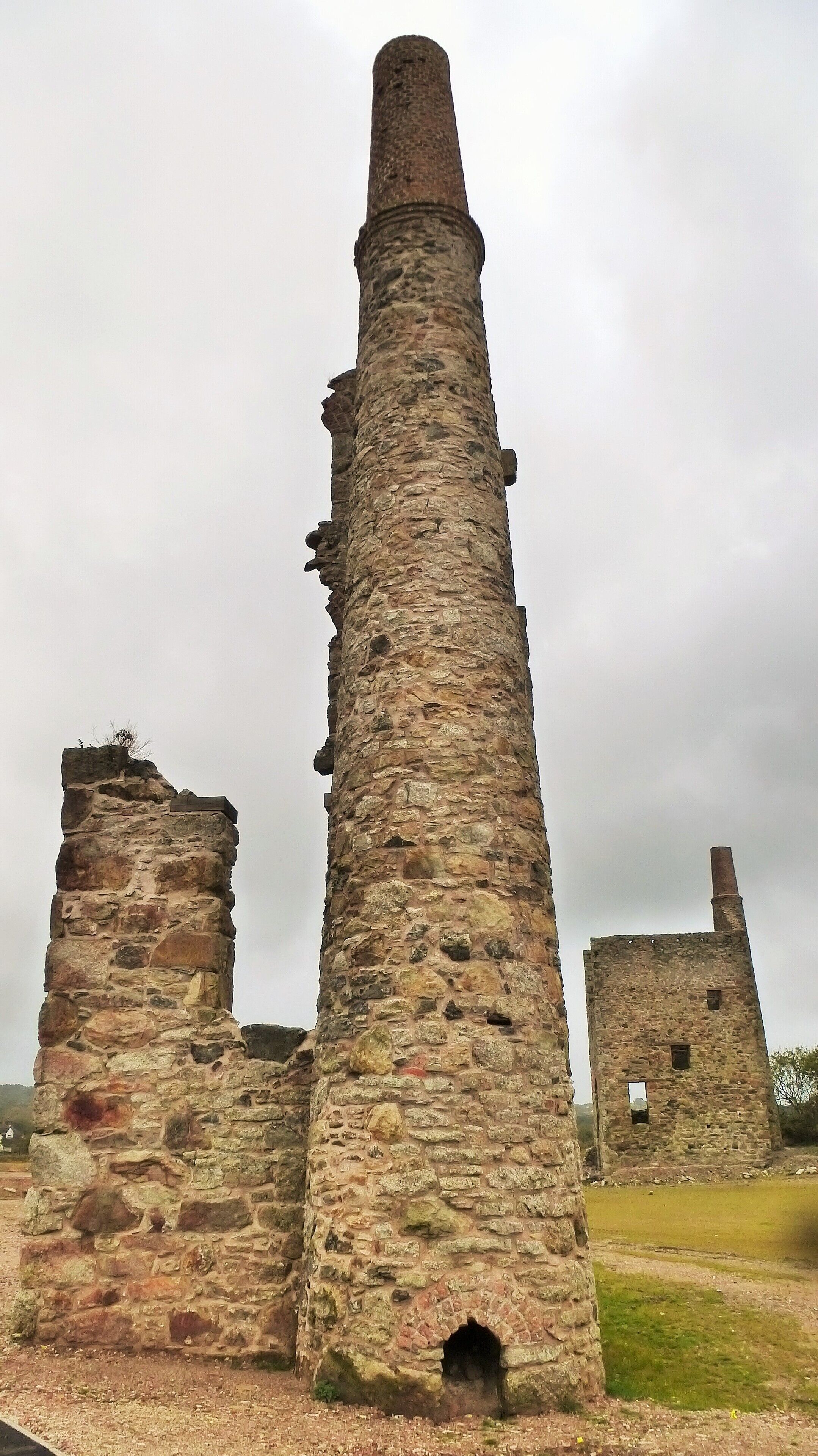 A tall, weathered stone tower with a narrow top, surrounded by other ruins.