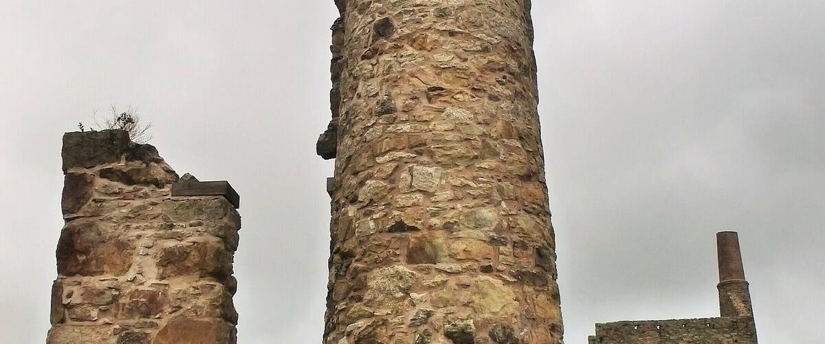 A tall, weathered stone tower with a narrow top, surrounded by other ruins.