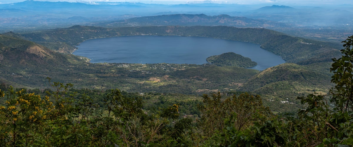 A panoramic view of a lake surrounded by mountains and dense forest.