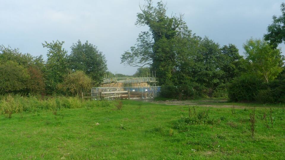 A grassy field with a metal structure and trees in the background.