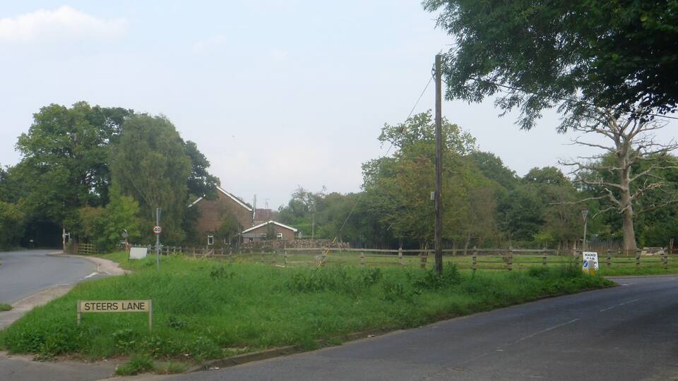 A rural road with a 'Steers Lane' sign, a speed limit sign, and a 'Hand Brake' sign.