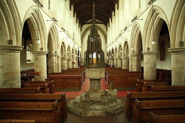 A church interior with wooden pews, stone columns, and a central altar.
