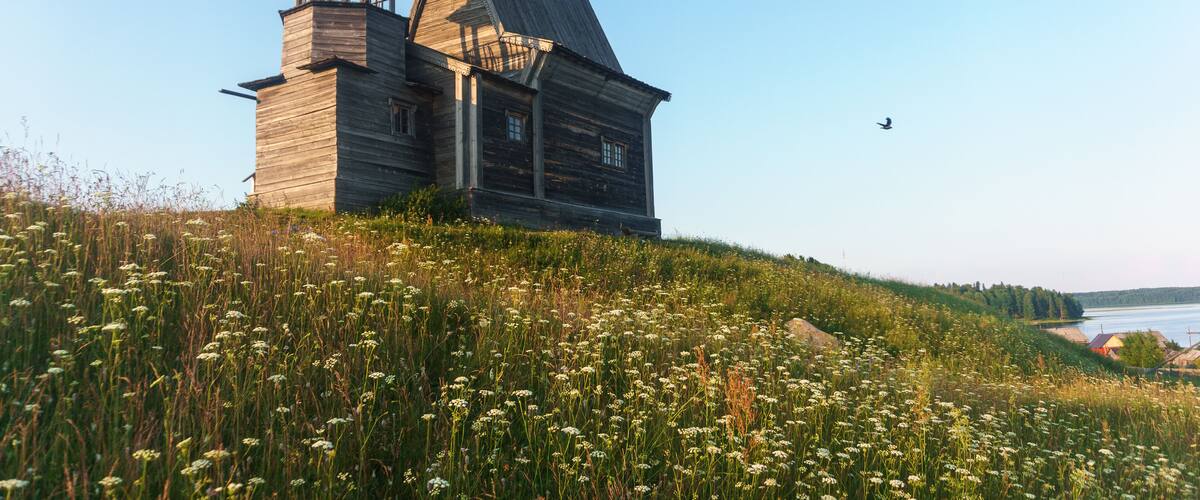 A wooden church with a bell tower and two domes, surrounded by a field of wildflowers.