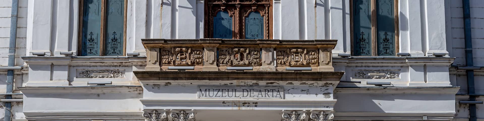 A white building with ornate carvings and three flags.