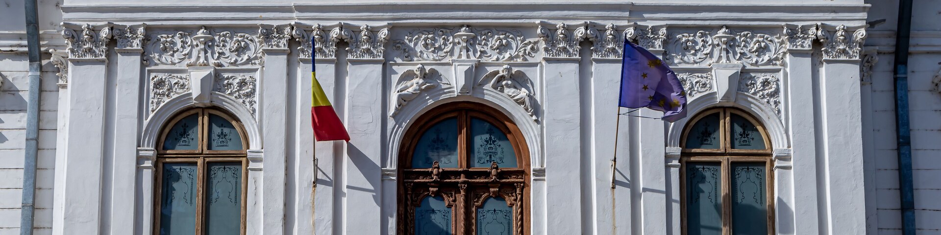Edifício branco com esculturas elaboradas e três bandeiras.
