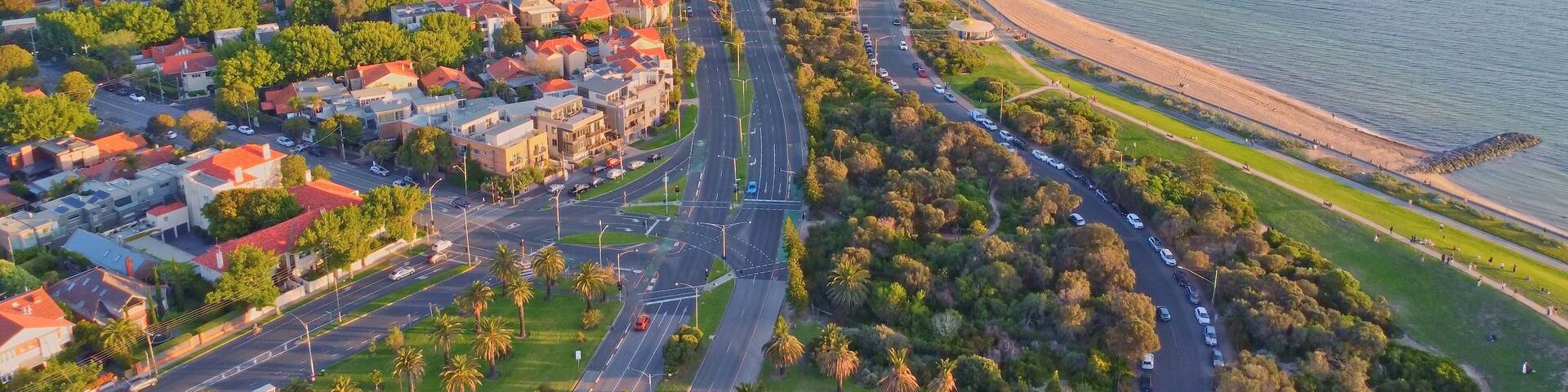 Golden Hour Aerial View of Melbourne's Bayside Coastline with Sandy Beach, Palm-Lined Roads, and Residential Suburbs