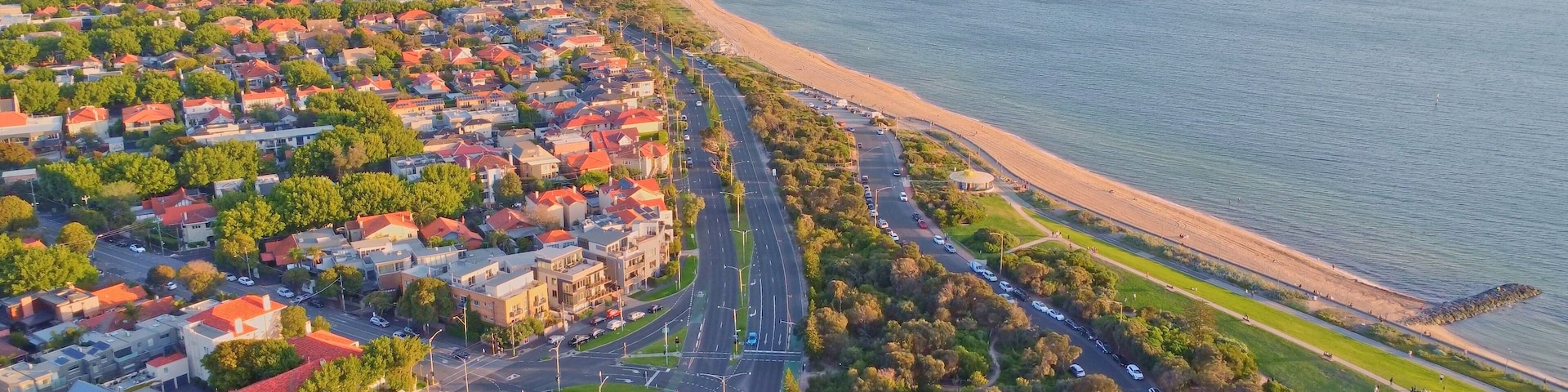 Golden Hour Aerial View of Melbourne's Bayside Coastline with Sandy Beach, Palm-Lined Roads, and Residential Suburbs