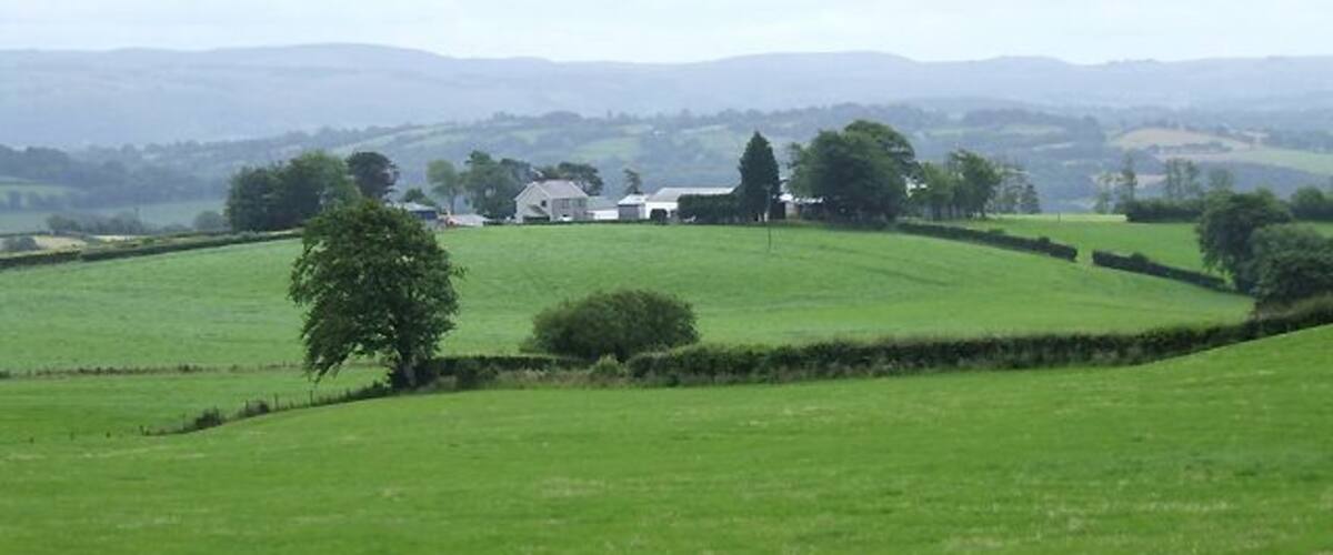 Rolling green hills, a farmhouse, and distant hills.