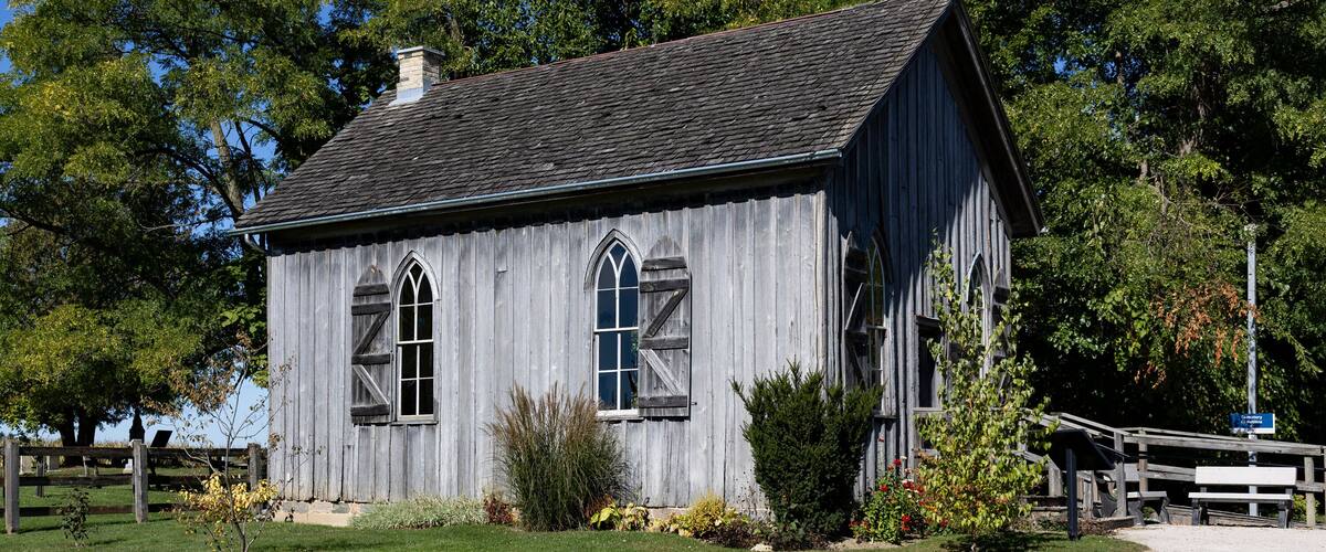 A rustic wooden building with a steeply pitched roof and arched windows, surrounded by a well-maintained lawn and a wooden fence.