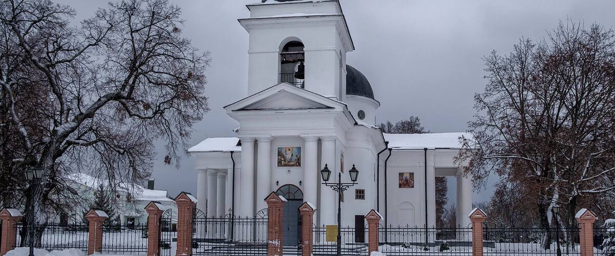 A white church with a tall steeple and a dome, surrounded by snow-covered trees.