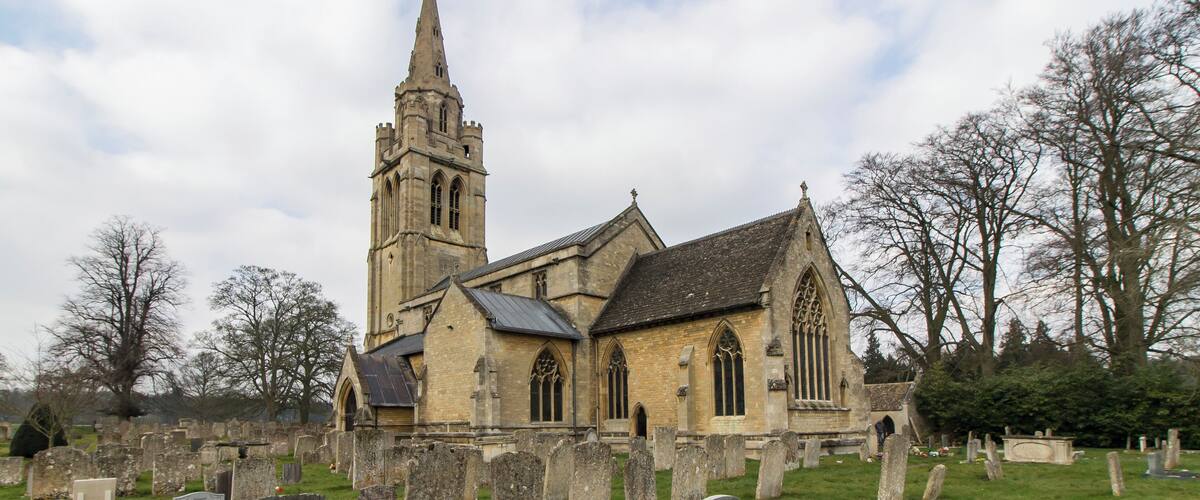 A historic church with a tall spire and a graveyard in front.