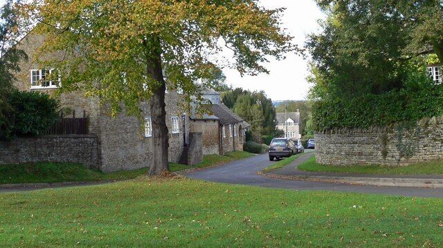 A narrow road in a rural area with stone walls, houses, and trees.