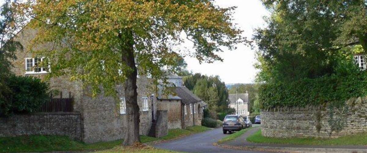 A narrow road in a rural area with stone walls, houses, and trees.