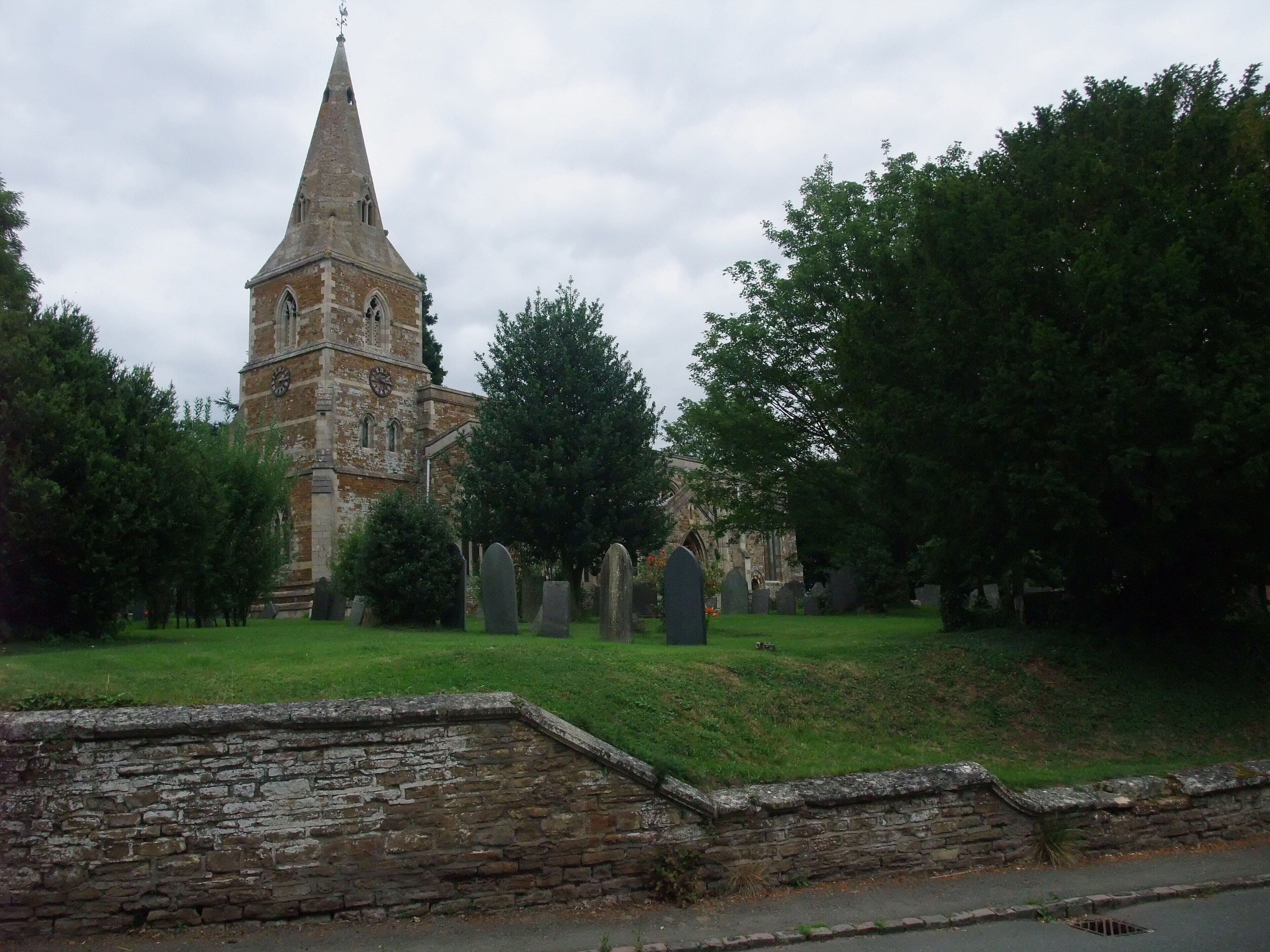 A church with a tall spire, surrounded by a cemetery with headstones.