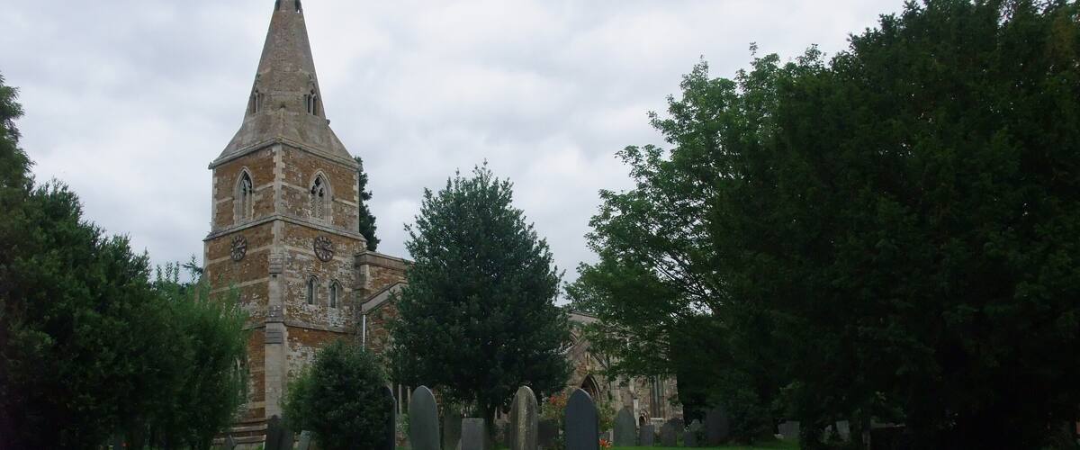 A church with a tall spire, surrounded by a cemetery with headstones.