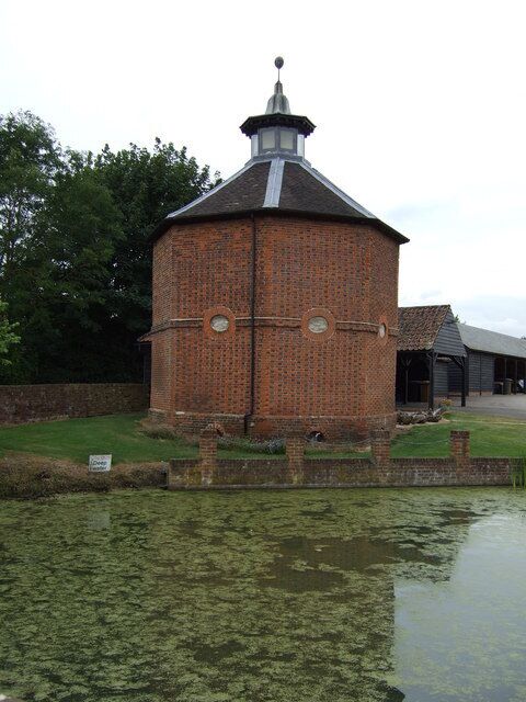 A brick tower with a conical roof and a clock, surrounded by a pond and greenery.