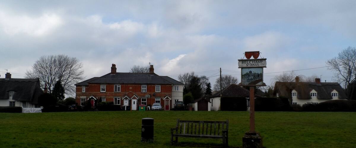 A grassy field with a bench, a signpost, and a red brick building in the background.
