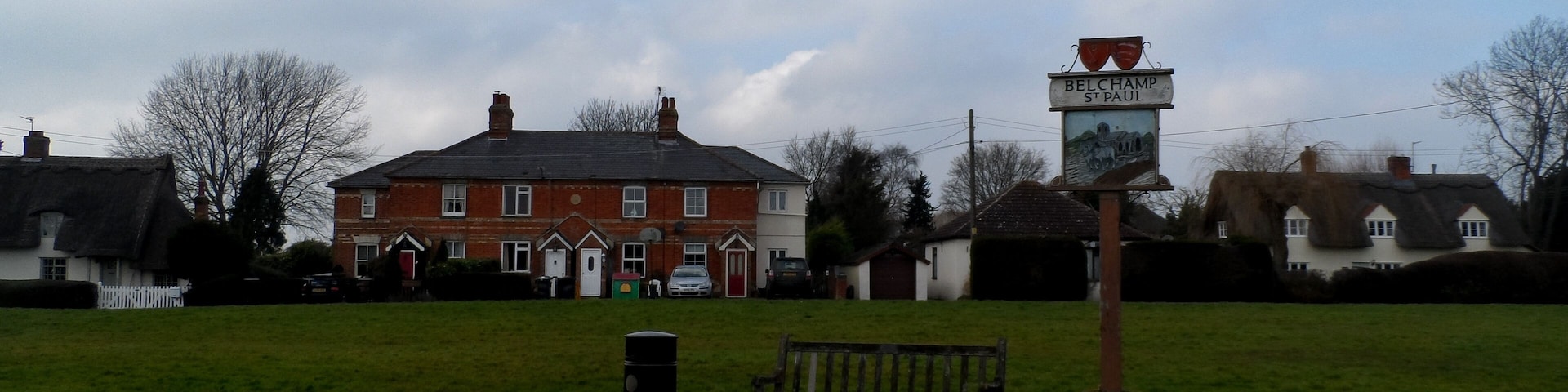 A grassy field with a bench, a signpost, and a red brick building in the background.