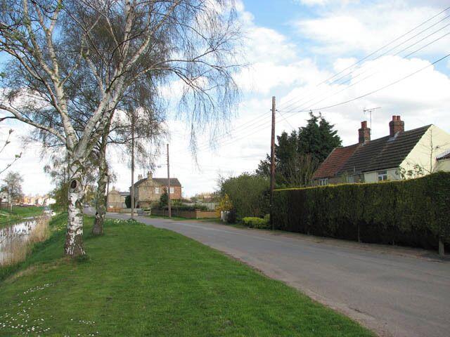 Low Side Northeasterly view along Low Side which runs parallel with the old course of the River Nene (seen at left). After leaving Wisbech & Upwell tramway's Upwell depot > https://www.geograph.org.uk/photo/1241222 - the line's southern terminus - the trains headed northwards > https://www.geograph.org.uk/photo/1241251 to the village of Outwell, crossing Small Lode > https://www.geograph.org.uk/photo/1241268 and passing a farm before emerging on Low Side which was the final request stop. A farm driveway now runs where the railway trackbed used to be > > https://www.geograph.org.uk/photo/1241431. Low side is the name of the road with runs parallel with the old course of the River Nene - the tram followed this road's eastern verge. http://www.lner.info/co/GER/wisbech/route.shtml When during the 13th century the estuary silted up, the fens surrounding the market town and port of Wisbech were reclaimed for agricultural use. The new agricultural prosperity soon attracted railways such as the Eastern Counties Railway which opened a branch in 1847. In 1848 the East Anglian Railway built a branch from Watlington. A third line was built by the Peterborough, Wisbech & Sutton Bridge Railway (later the Midland & Great Northern Joint Railway) which opened a station on the other side of the River Nene in 1866. The trains carried fruit and vegetables to markets as far afield as London. In addition, the construction of a tramway line connecting the villages Upwell and Outwell with Wisbech commenced in 1882. Board of Trade's tram restrictions resulted in the unusual-looking locomotives which not only had speed restrictions but controls at both ends and wooden cowcatchers and skirts over the wheels. Six trams a day in each direction provided passenger services, with the full one way journey taking one hour. By October 1884 traffic had grown to 3000 passengers per week, with peaks of 2000 in a day for fetes and other special events. The tram competed with a canal that ran between Wisbech and Upwell and with the canal being in a poor financial condition the tram eventually finished it off. When motor omnibuses started to appear, however, passenger numbers declined drastically and passenger services were withdrawn in 1927, whereas freight traffic continued to flourish. With the introduction of two Drewry Shunters (BR Class 04) in 1952, Wisbech & Upwell became Britain's first all-diesel line. The line closed in March 1966. http://www.lner.info/co/GER/wisbech/history.shtml