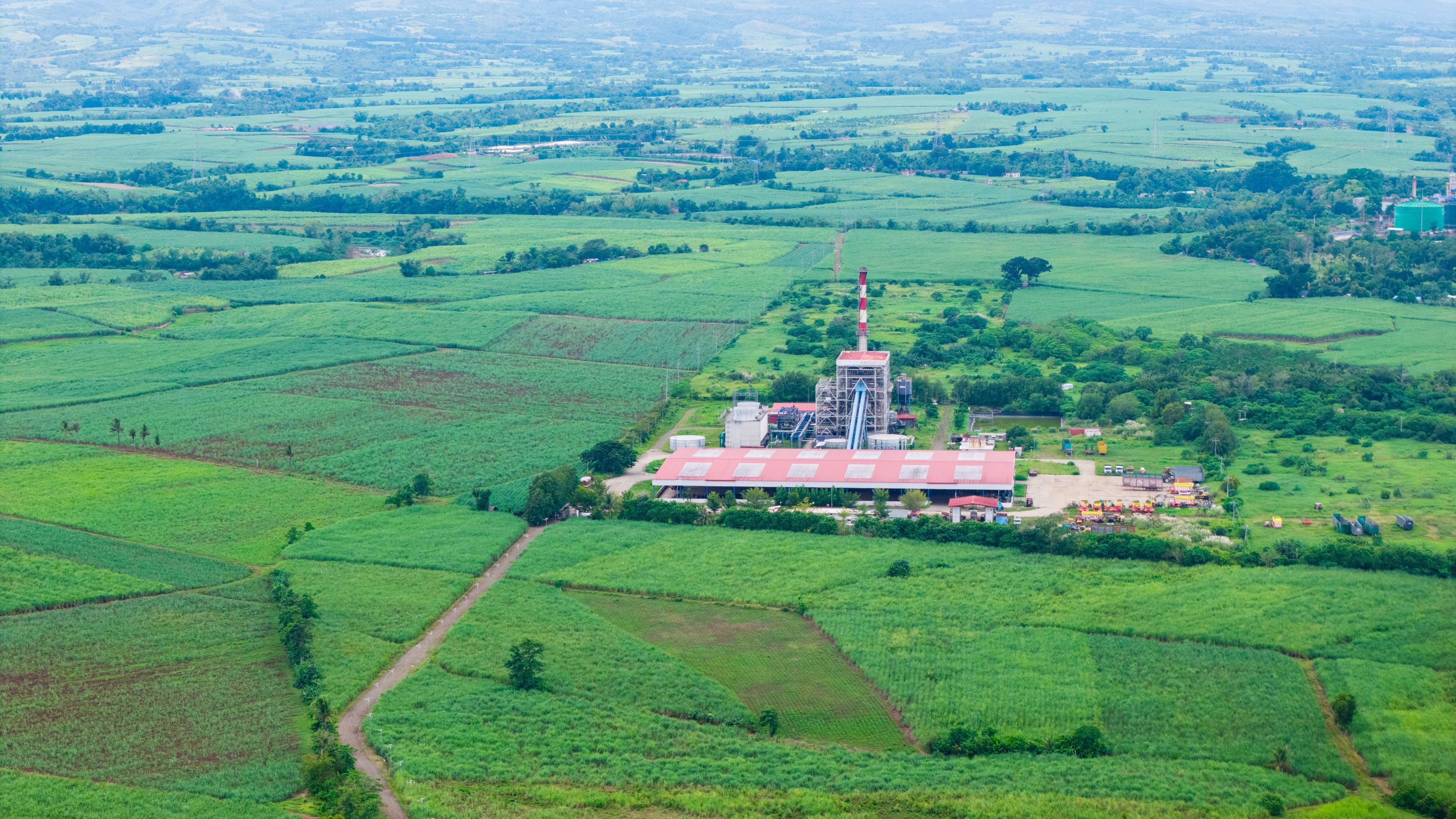 An agricultural landscape with fields, a large building with a red roof, and a tall structure with a red and white tower.