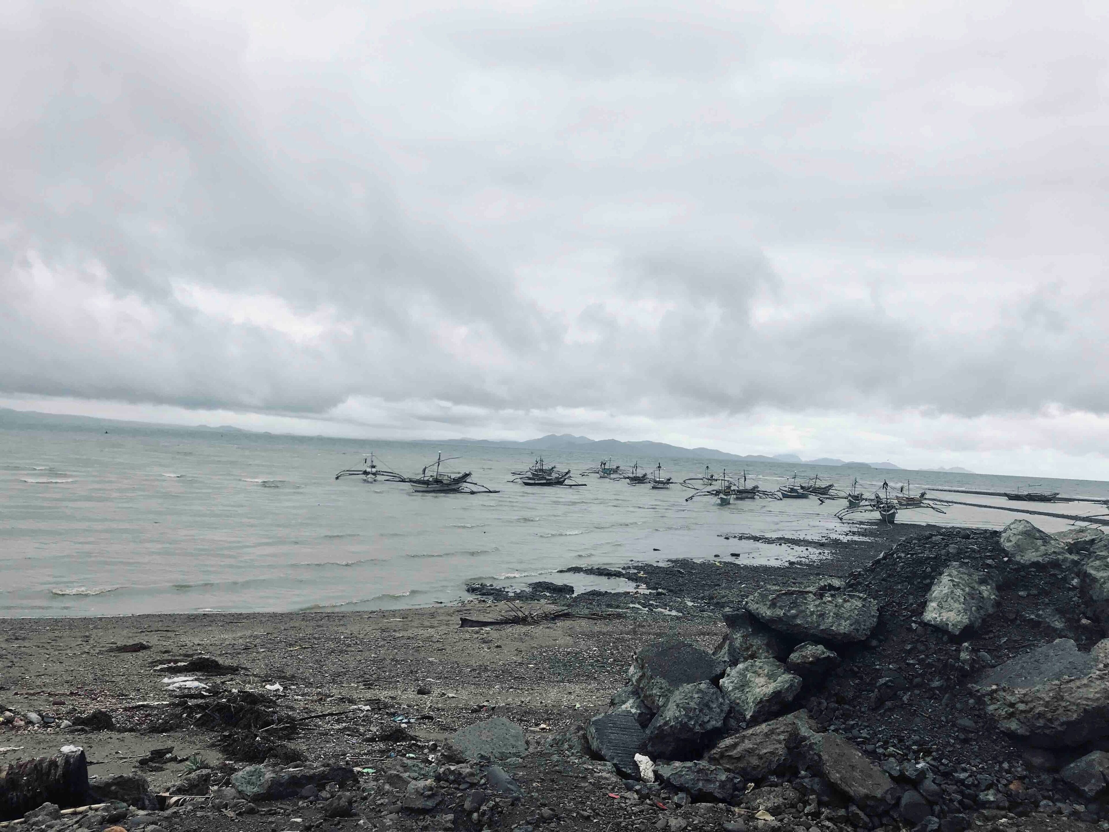 A rocky shoreline with several traditional boats anchored in the water.