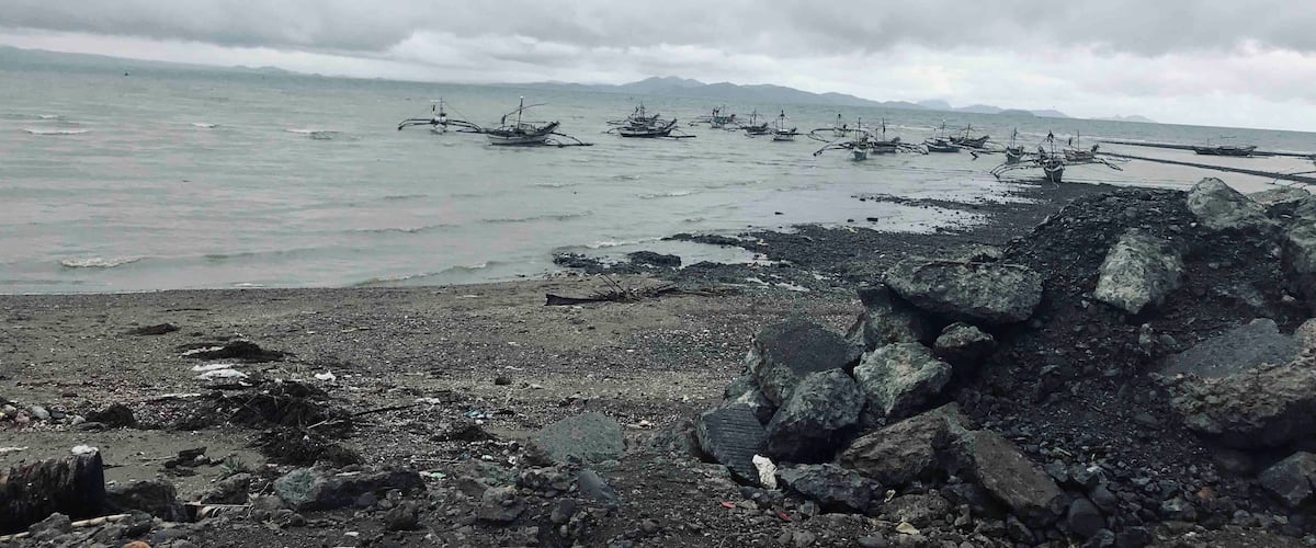 A rocky shoreline with several traditional boats anchored in the water.