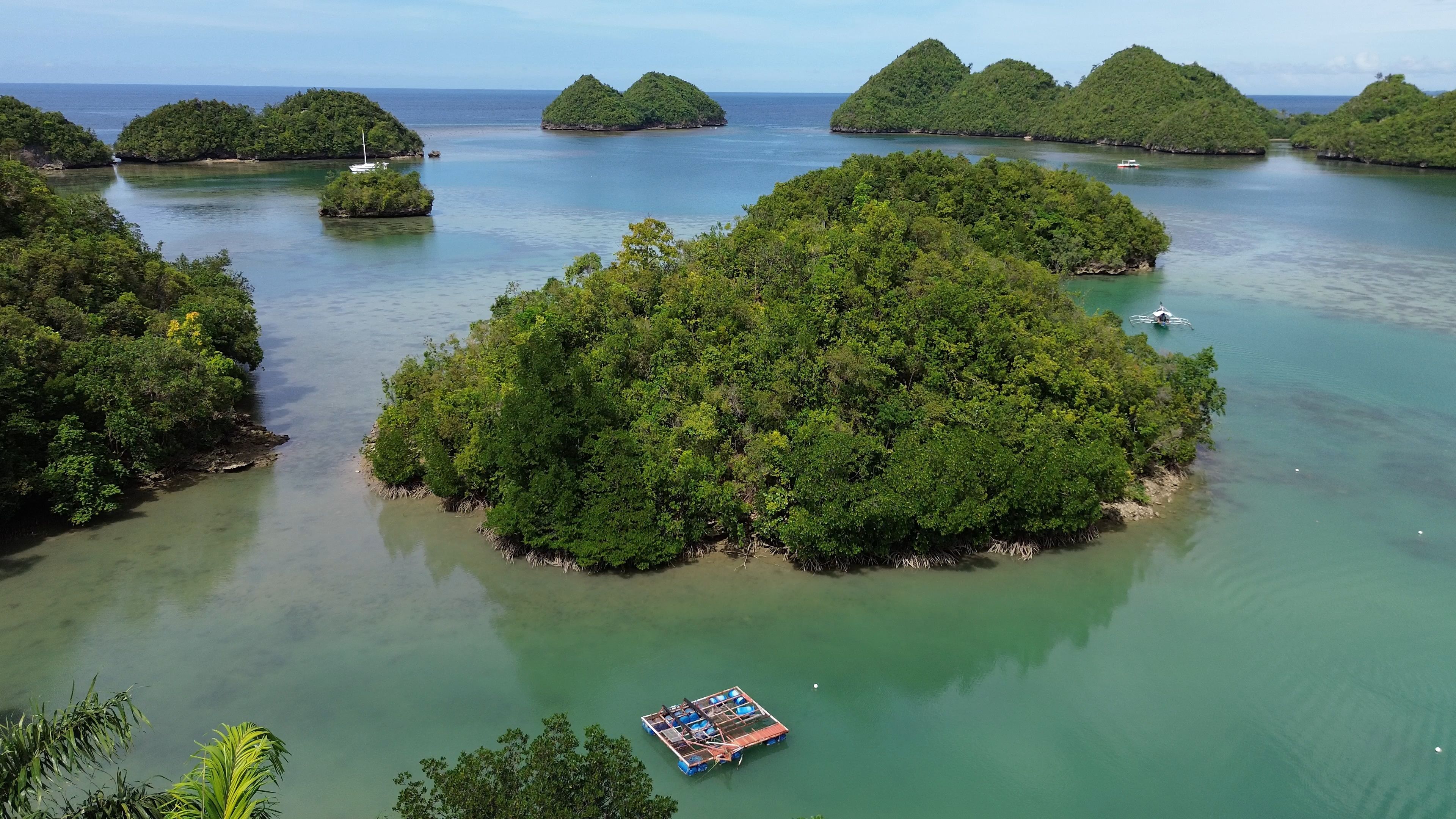 A tropical island surrounded by clear waters with a small boat anchored nearby.