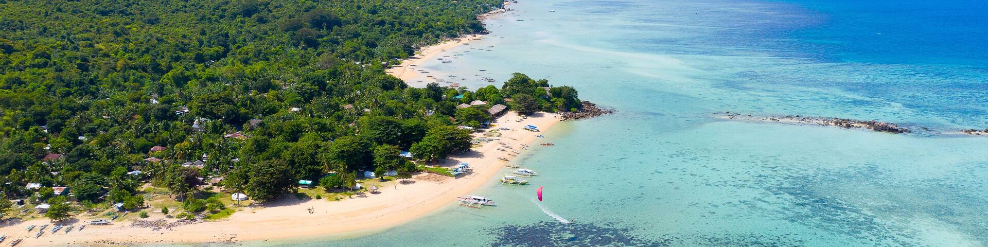 A tropical beach with clear turquoise waters, a sandy shore, and lush green hills in the background.