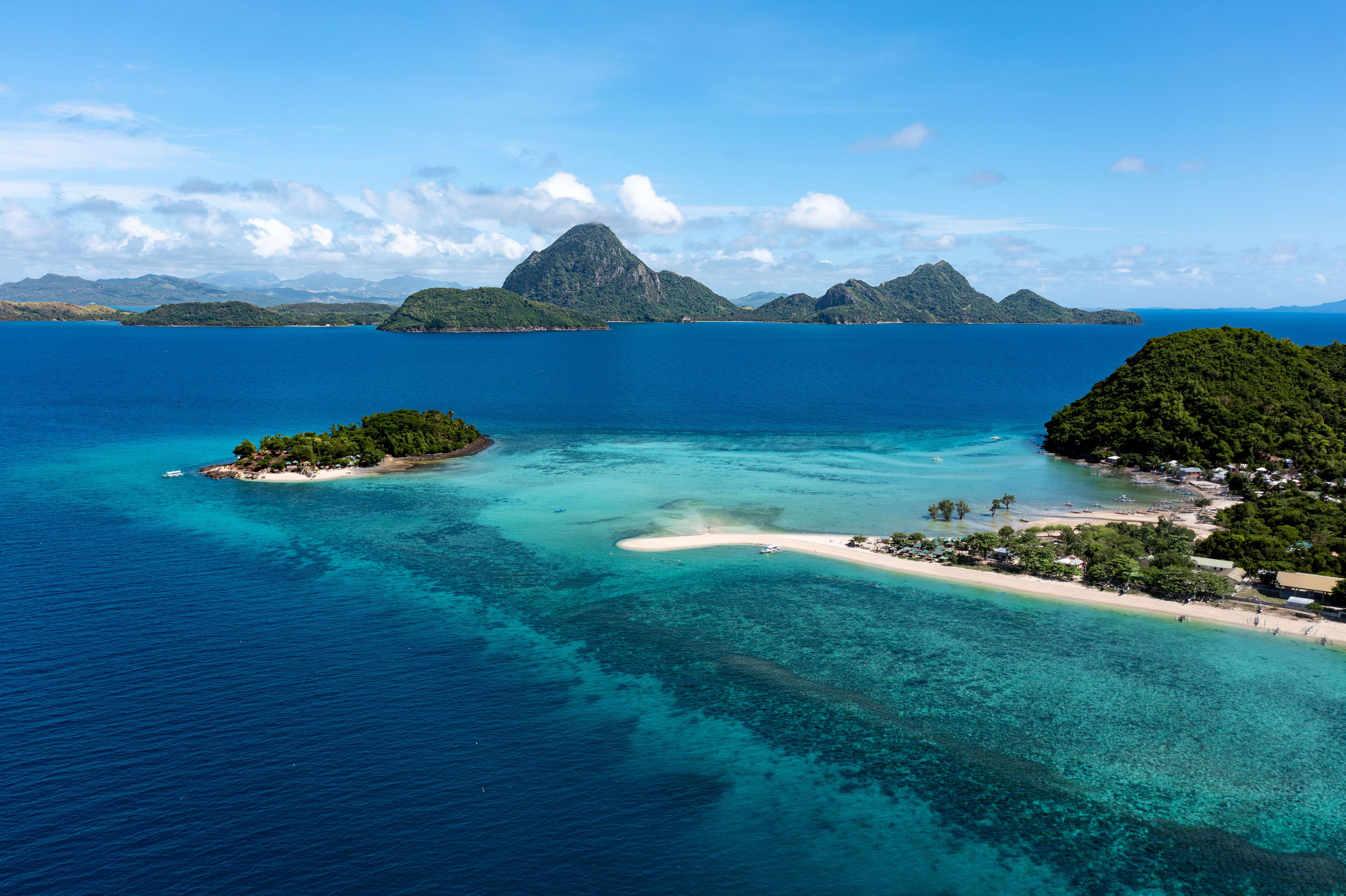 Eine tropische Insel mit klarem türkisblauem Wasser, einem Sandstrand und üppigen grünen Hügeln im Hintergrund.