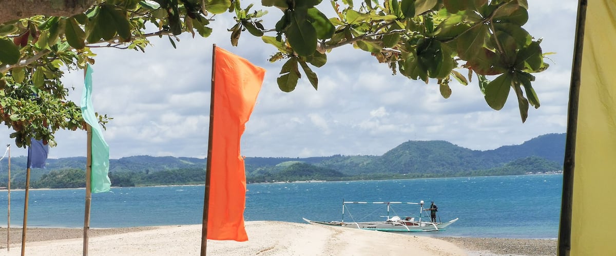 A beach with a boat on the water, flags, and a mountainous landscape in the background.