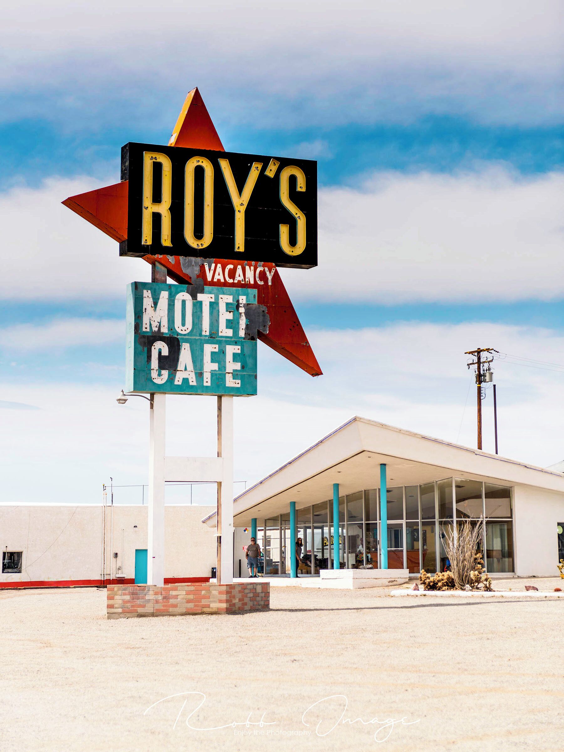 A motel sign with 'ROY'S' and 'VACANCY' in yellow letters, and 'MOTEL CAFE' in white letters on a teal background.