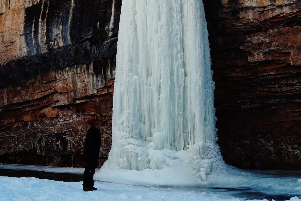 A person standing in front of a large waterfall of ice.