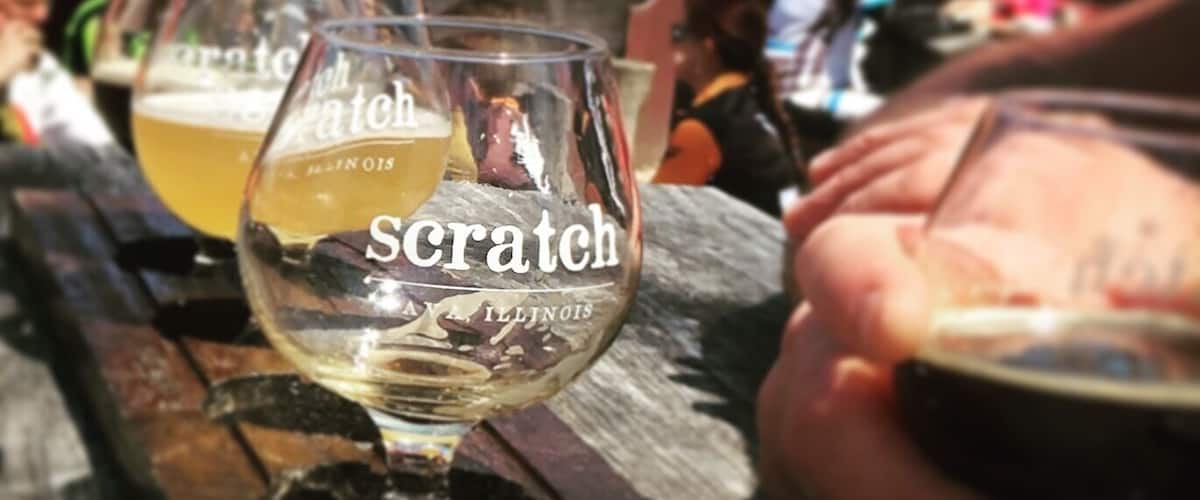 A wooden table with several glasses of beer, one prominently labeled 'scratch' with 'Illinois' visible.