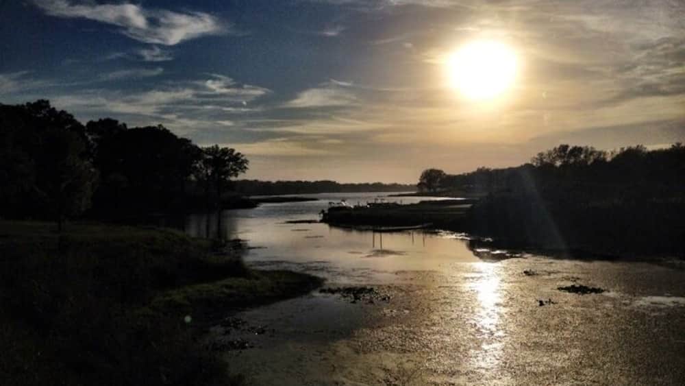 A river at sunset with the sun low on the horizon, reflecting on the water.