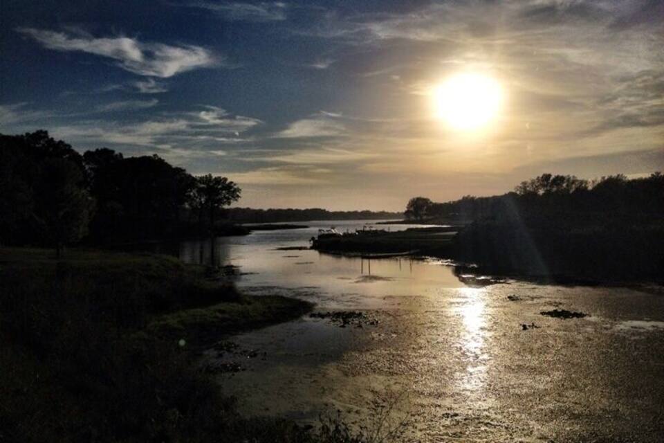 A river at sunset with the sun low on the horizon, reflecting on the water.