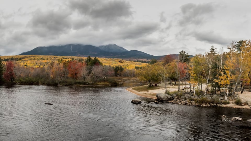 A calm river with autumn foliage and mountains in the background.