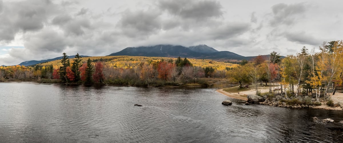 A calm river with autumn foliage and mountains in the background.