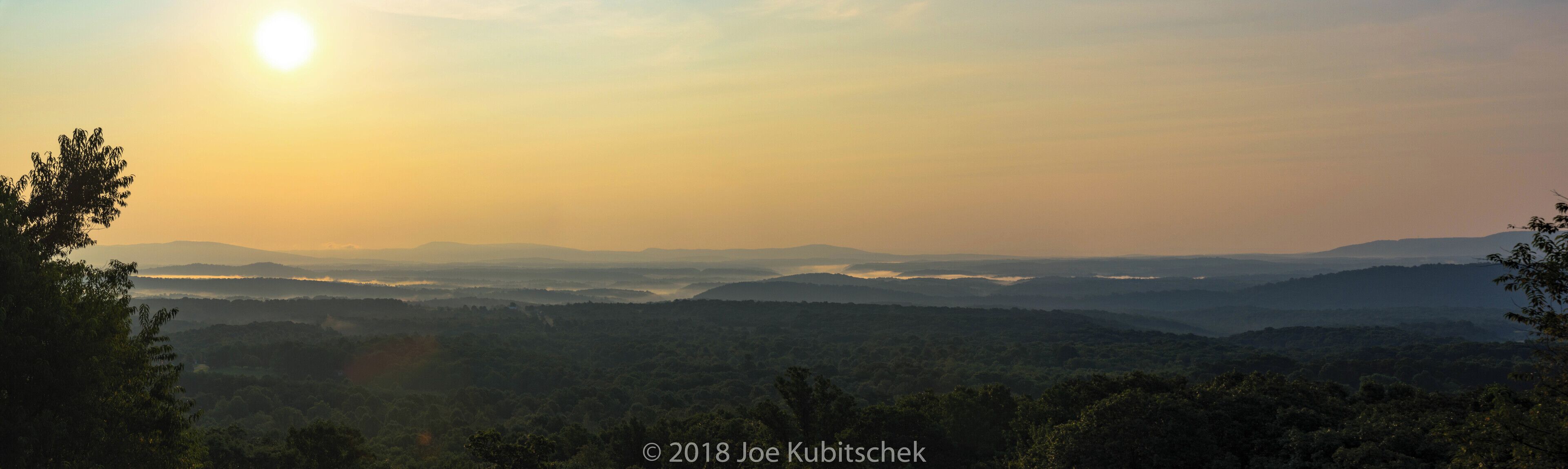 A sunrise over a mountainous landscape with dense forests.