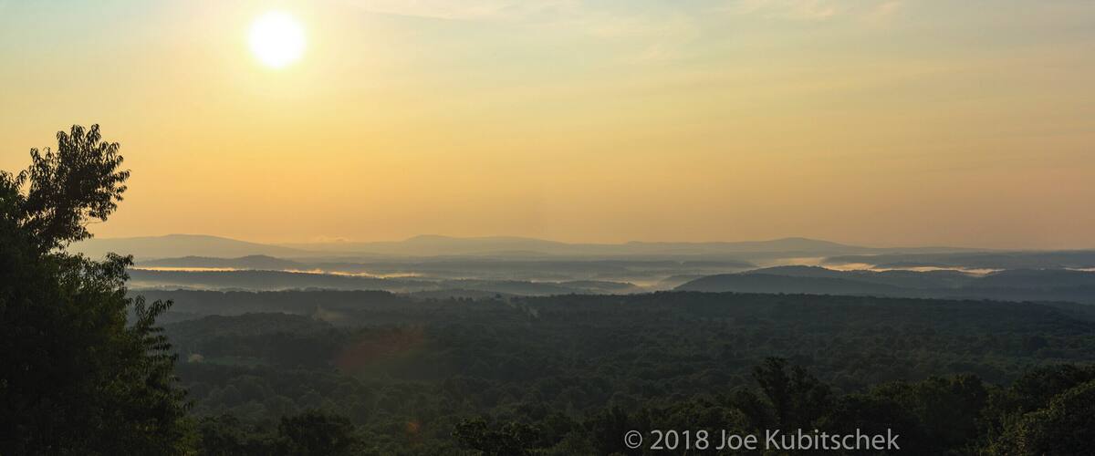 A sunrise over a mountainous landscape with dense forests.