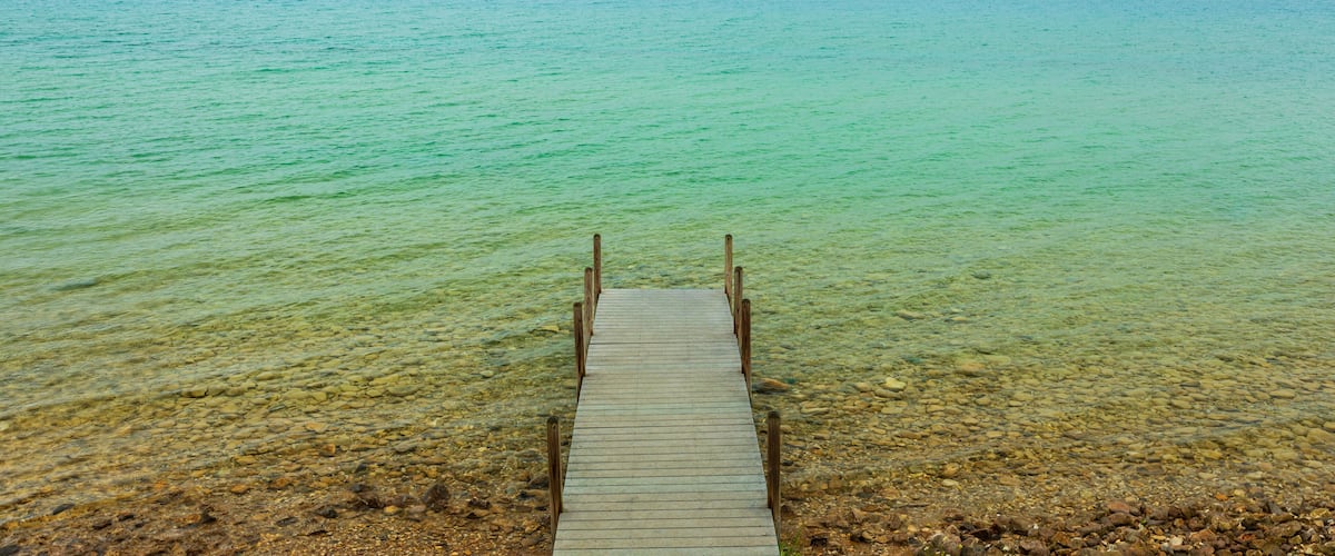A wooden pier extending into a calm, turquoise lake surrounded by rocky terrain.