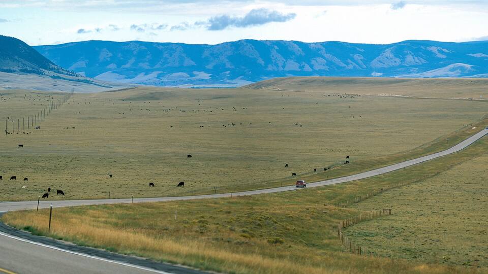 A winding road through a vast, open field with distant mountains.