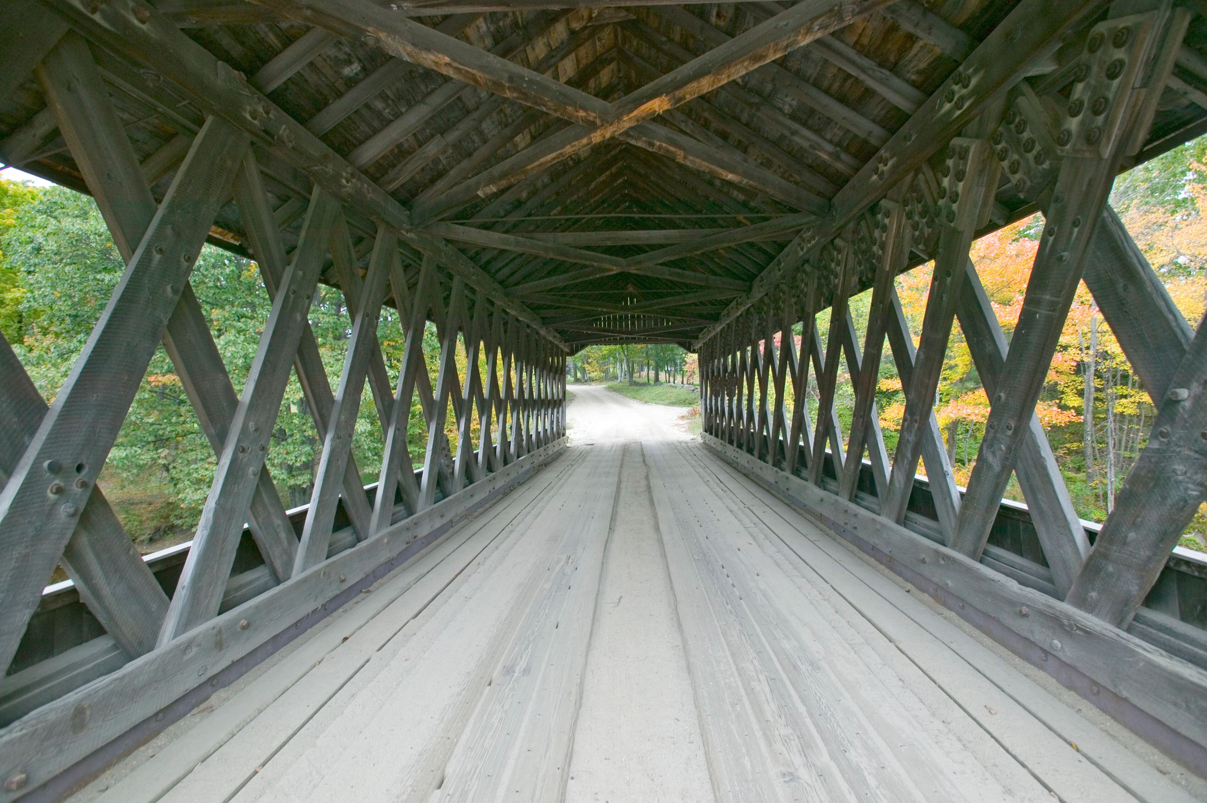 A wooden covered bridge with a metal railing, surrounded by trees with autumn foliage.