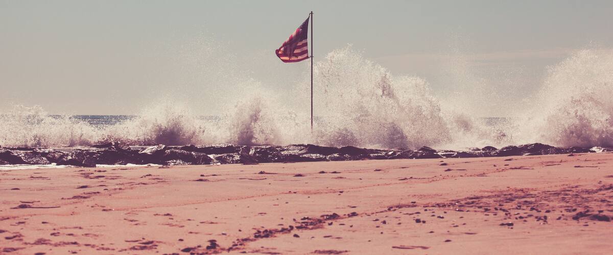 A beach with waves crashing onto rocks and a flagpole with a flag.