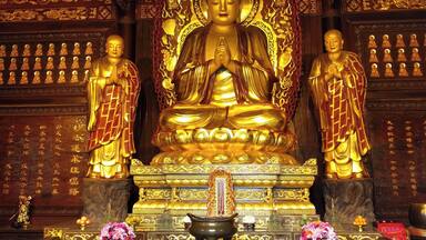 Una gran estatua dorada de Buda rodeada de estatuas más pequeñas, elaboradas esculturas y ofrendas.