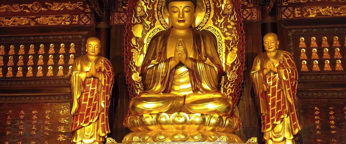A large golden Buddha statue surrounded by smaller statues, ornate carvings, and offerings.