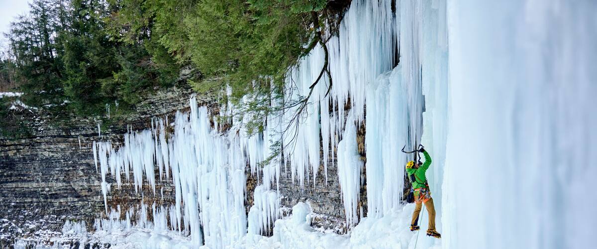 A person ice climbing on a frozen waterfall surrounded by snow and trees.